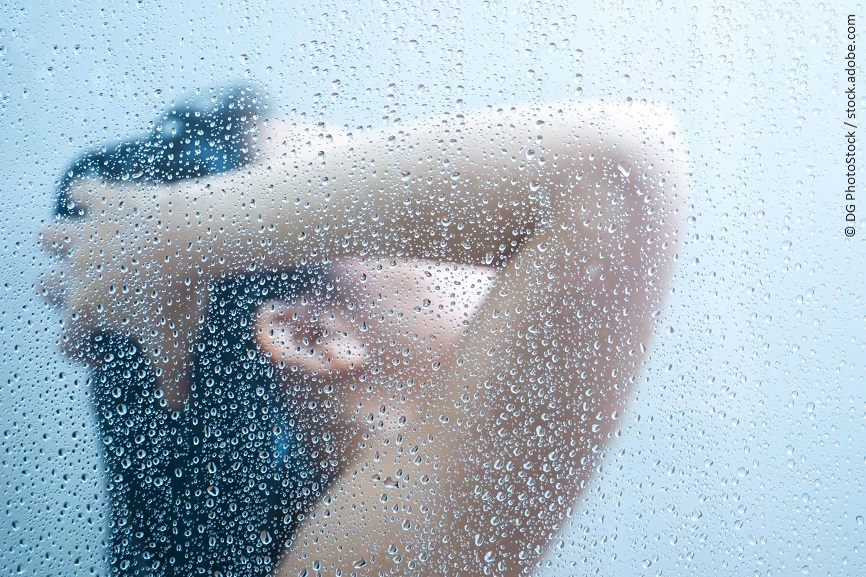 Eine beschlagene Duschwand aus Glas. Dahinter steht eine Person und wäscht sich die Haare. 